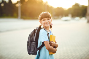 Smiling girl wearing a backpack and carrying a book