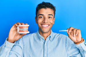 a patient holding a model of braces and Invisalign aligner